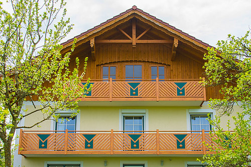 Balkongeländer vom Modell Gastein in anthrazit, montiert ist der Balkon auf einem modernen Holzhaus, links und rechts stehen Laubbäume