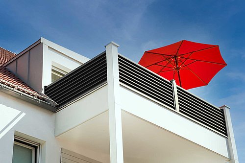 Balkongeländer aus Aluminium vom Modell Trento, ein großer roter Sonnenschirm ragt über den Balkon hinaus
