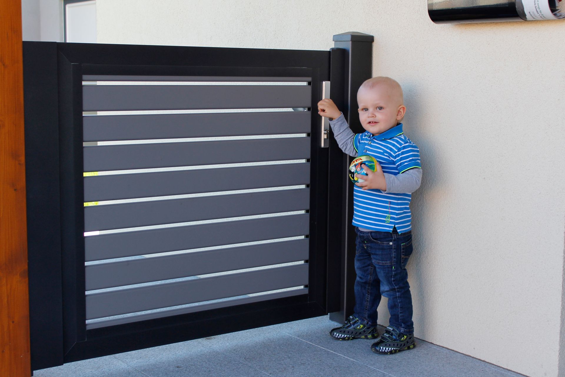 Gartentüre aus Latten in grau mit schwarzer Rahmenoptik, Modell Nouveau, Kleinkind öffnet die Gehtüre